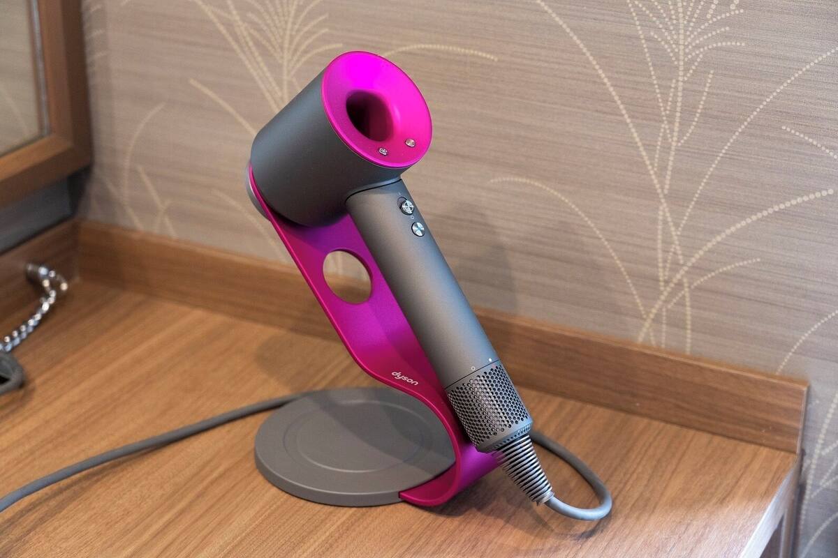 Un secador de pelo Dyson sobre una superficie de madera, con un papel tapiz estampado en el fondo.