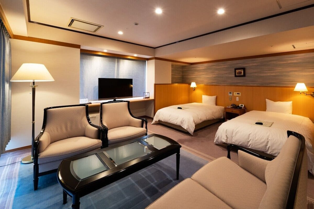 Una habitación de hotel con dos camas, televisor, escritorio y sofá.