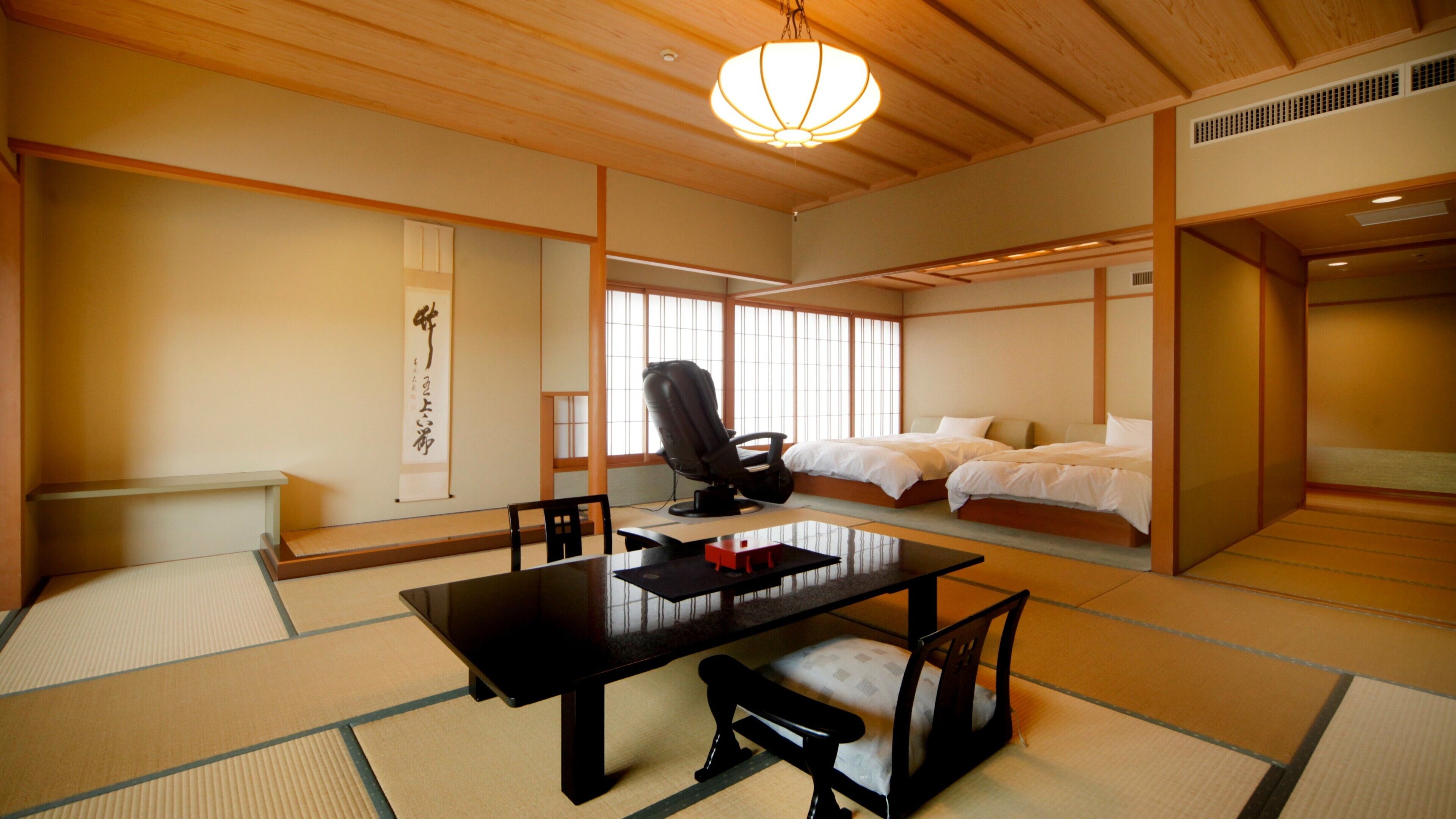 A traditional Japanese room with tatami flooring, a low table, a massage chair, and a bed with futons.