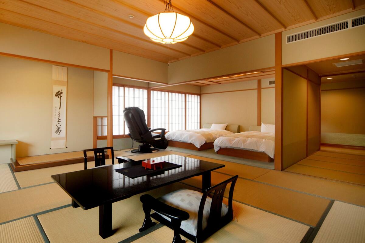 Una habitación japonesa tradicional con suelo de tatami, una mesita baja, una silla de masaje y una cama con futones.