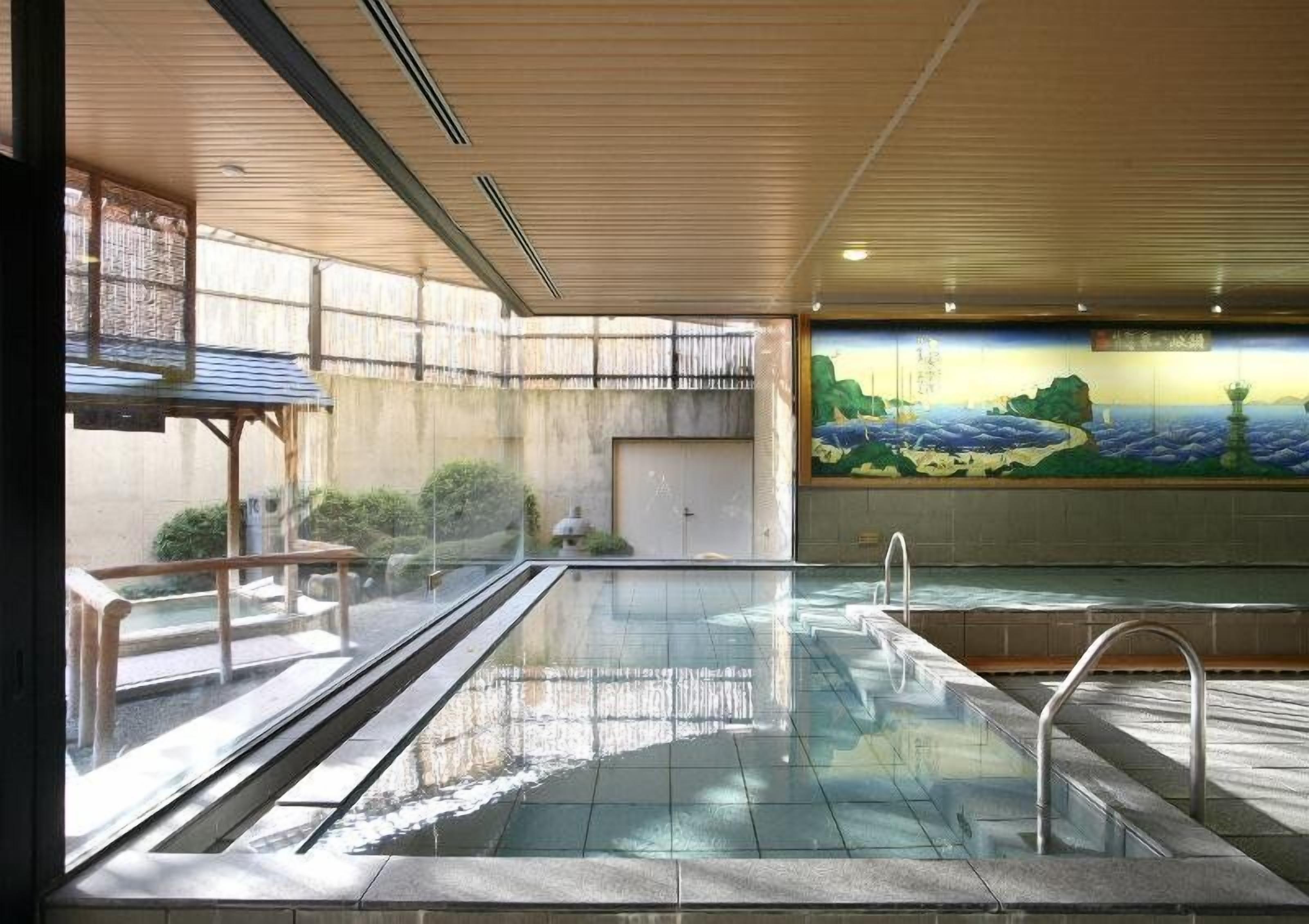 A swimming pool with a tiled floor, a metal handrail, and a mural on the wall.