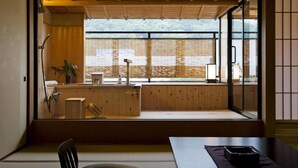 Una habitación japonesa tradicional con suelo de tatami, una mesa baja de madera, una puerta corredera de vidrio que da a un balcón y vistas a la montaña.
