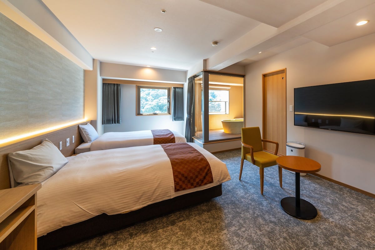 A hotel room with two beds, a TV, a small table, and a chair.