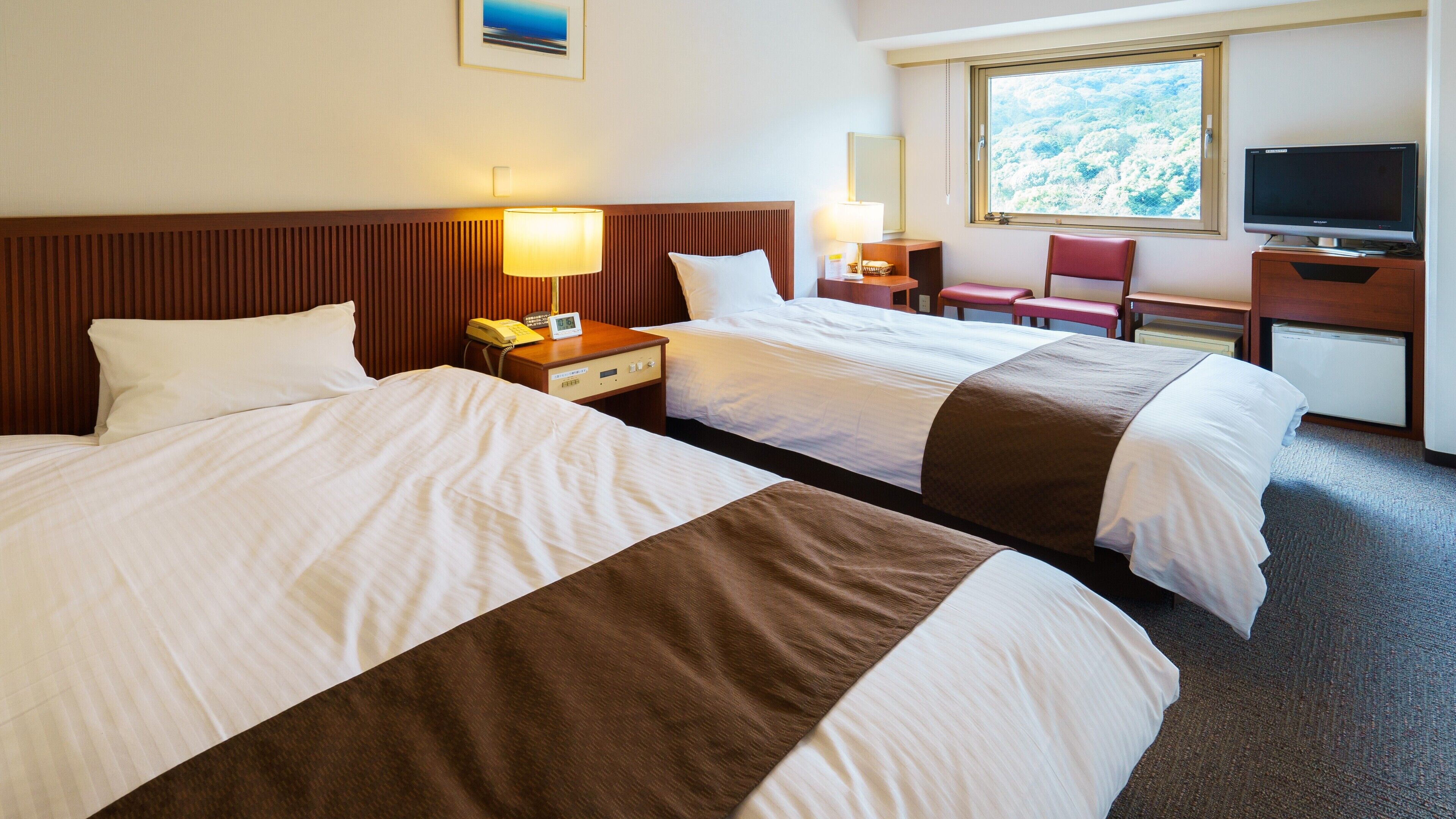 A hotel room with two beds, bedside lamps, a desk with a computer, a chair, and a TV.