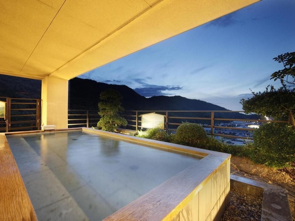 A rooftop pool with a view of mountains and a cityscape at dusk.