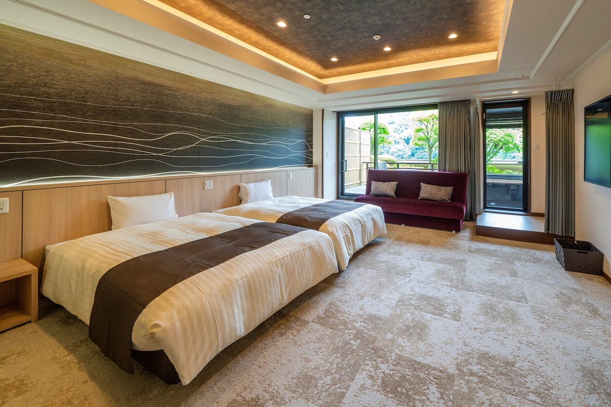 Habitación de hotel moderna con una cama grande, un sofá, un televisor y vistas a zonas verdes.