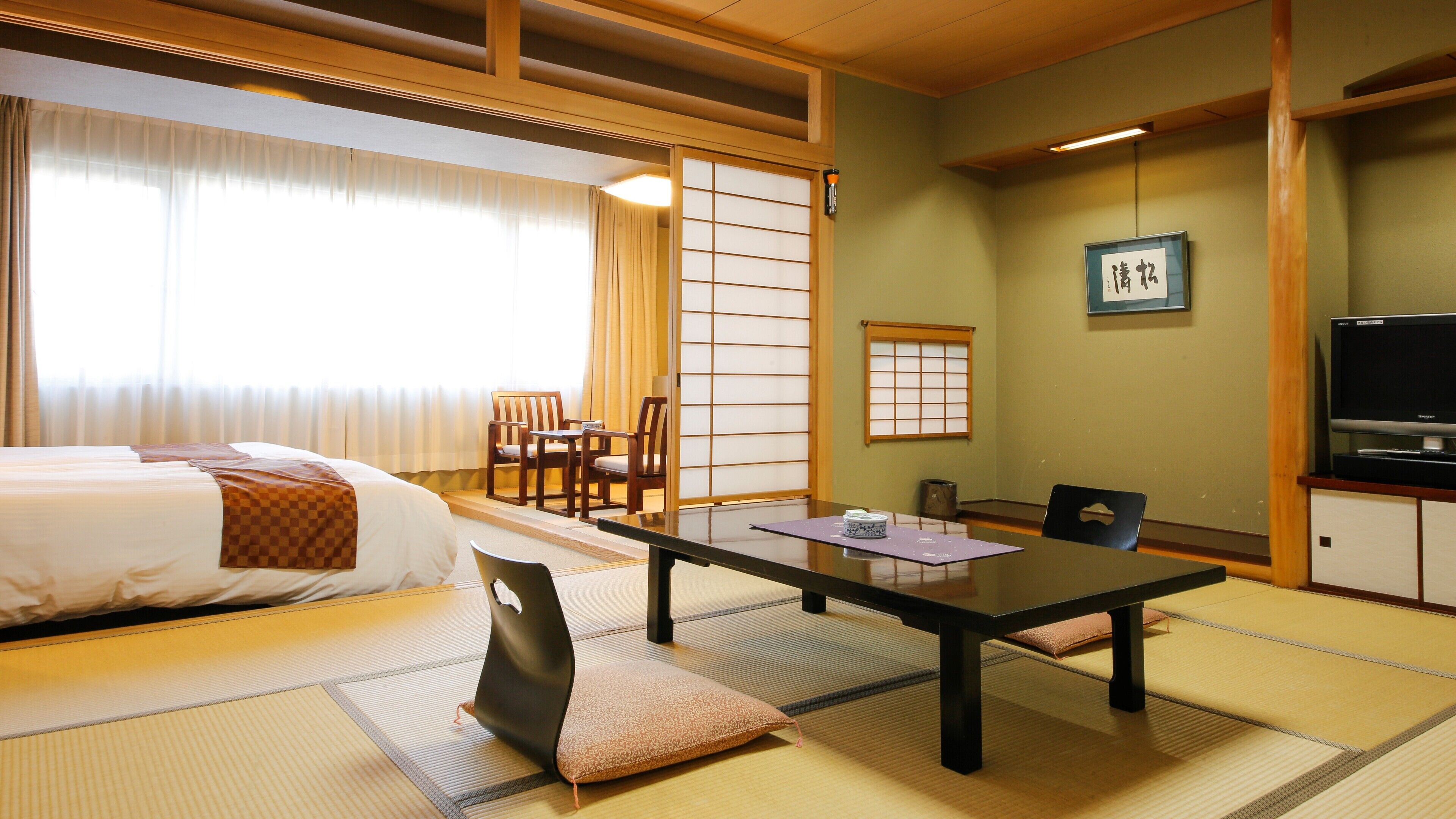A hotel room with a bed, a dining table, chairs, tatami mats, a television, and a shoji screen.