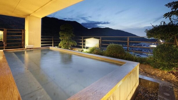 Piscina en la azotea con vistas a montañas y al paisaje urbano al atardecer.