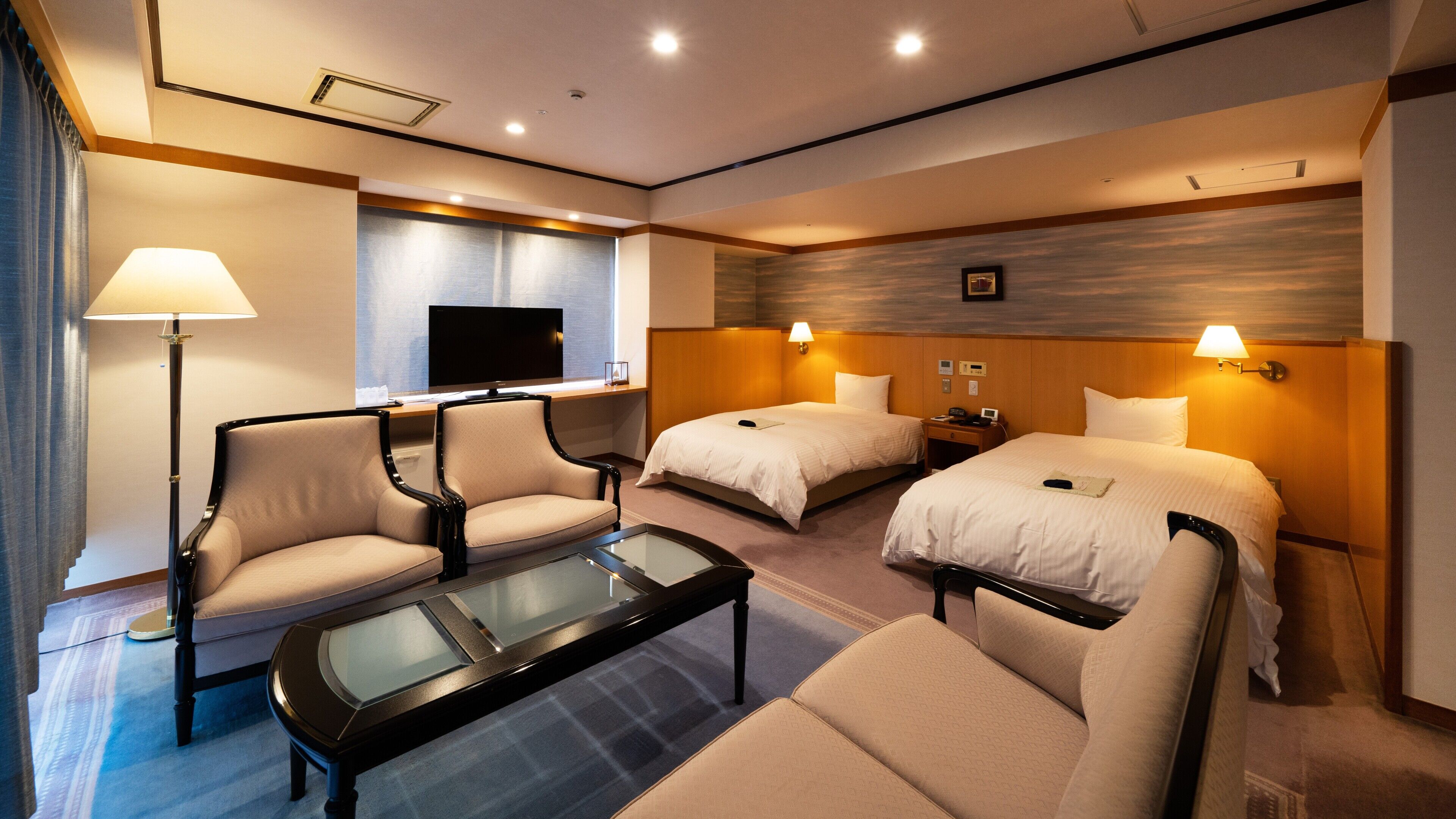 A hotel room with a sofa, two beds, a TV, a desk, and a lamp.