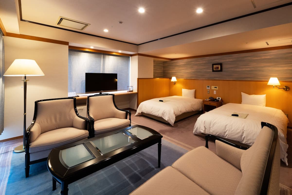 Habitación de hotel con sofá, dos camas, televisión, escritorio y lámpara.