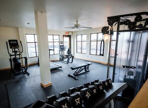 A gym with cardio machines, weightlifting equipment, and a ceiling fan.