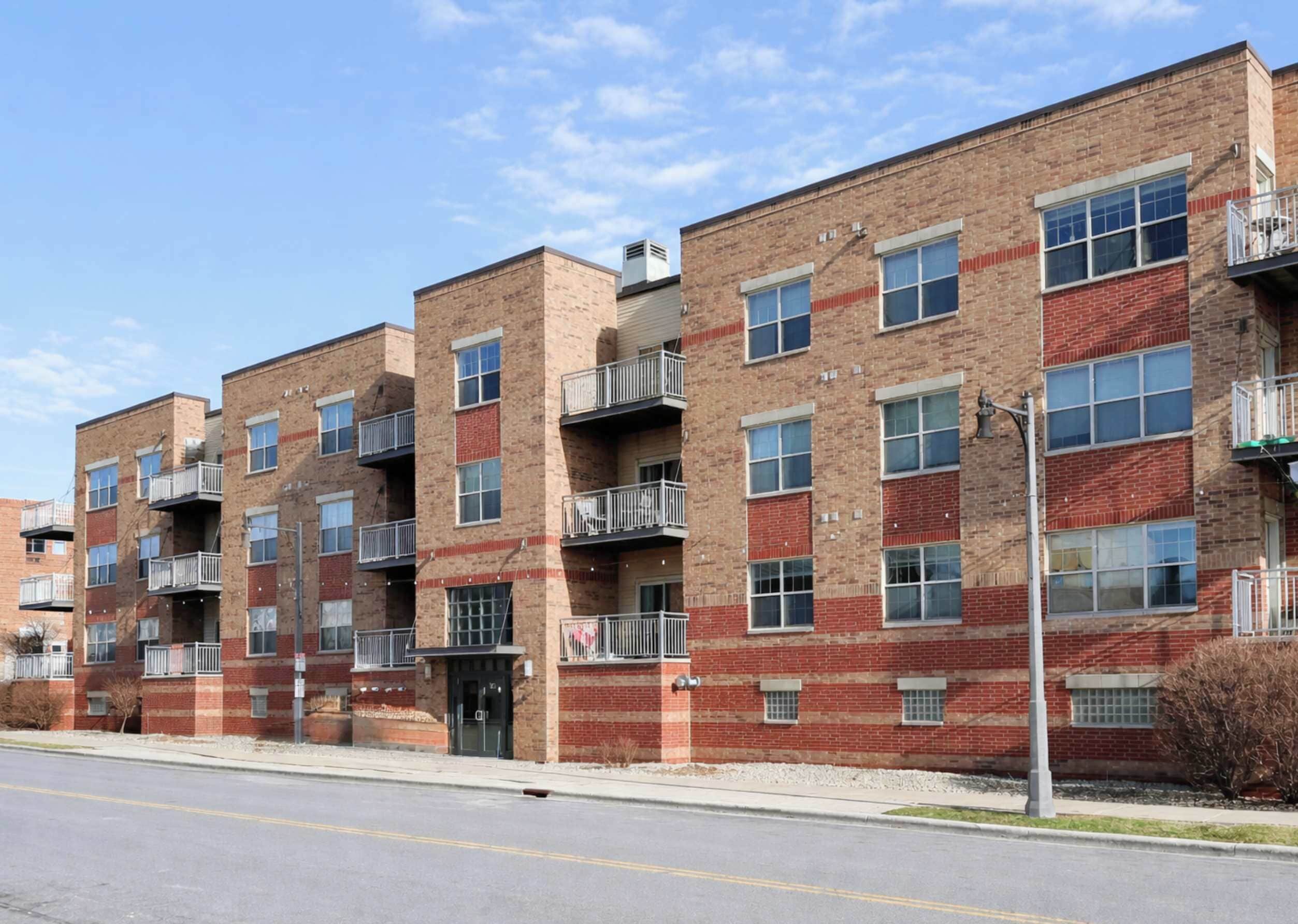 A multi-story brick building with balconies, a central entrance, and a clear sky.