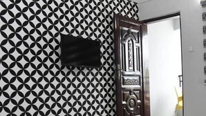 A room with a geometric patterned wallpaper, a black cabinet, and a wooden door with intricate designs.