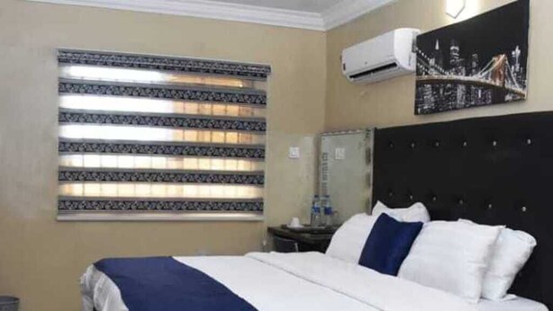 A hotel room with a bed, a nightstand, a mirror, and a window with blinds.