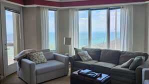 A spacious living room with two sofas, a coffee table, and large windows offering a view of the ocean. - View from the Top (Roseland)