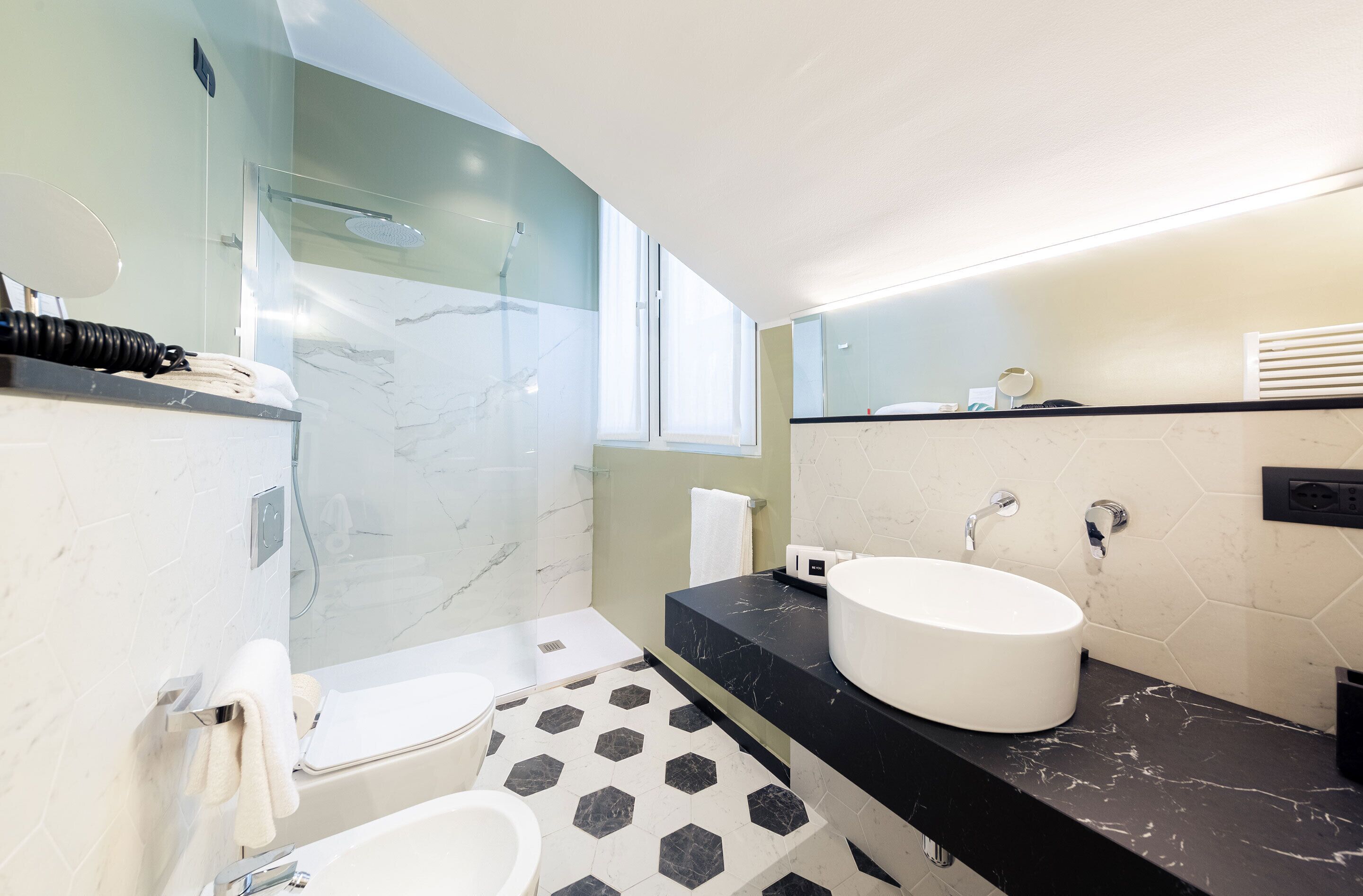 Een moderne badkamer met een douchecabine van glas, een witte wastafel en een zwart marmeren aanrecht.