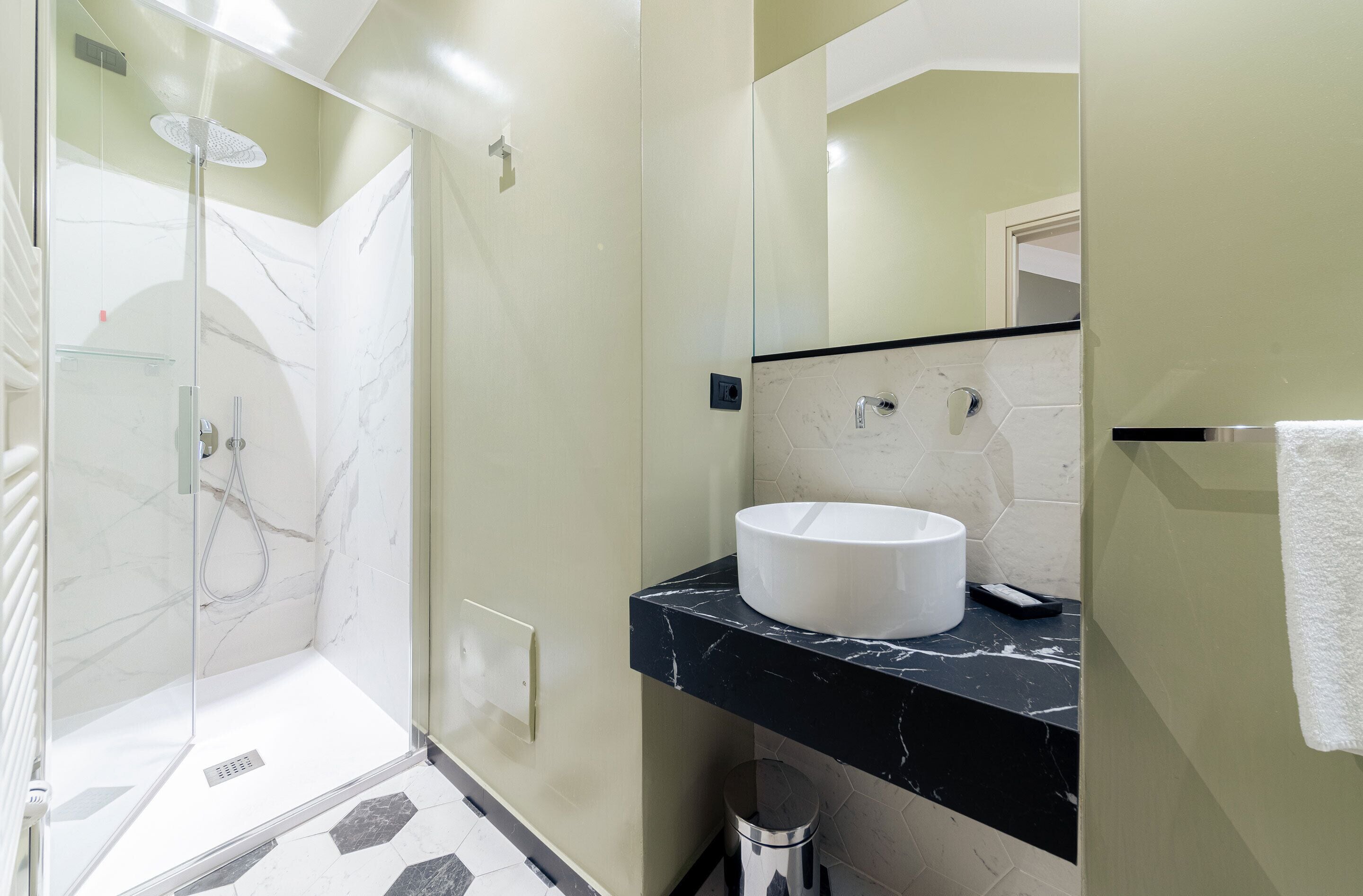 A modern bathroom with a glass-enclosed shower, a white sink, and a black marble countertop.