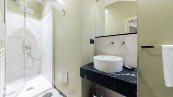 Un bagno moderno con doccia vetrata, un lavandino bianco e un piano d'appoggio in marmo nero.