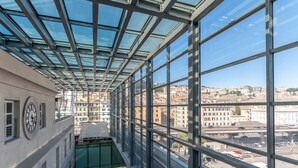 A high-rise building with large windows and a glass ceiling, offering views of a cityscape. - Hotel Astoria (Genoa)