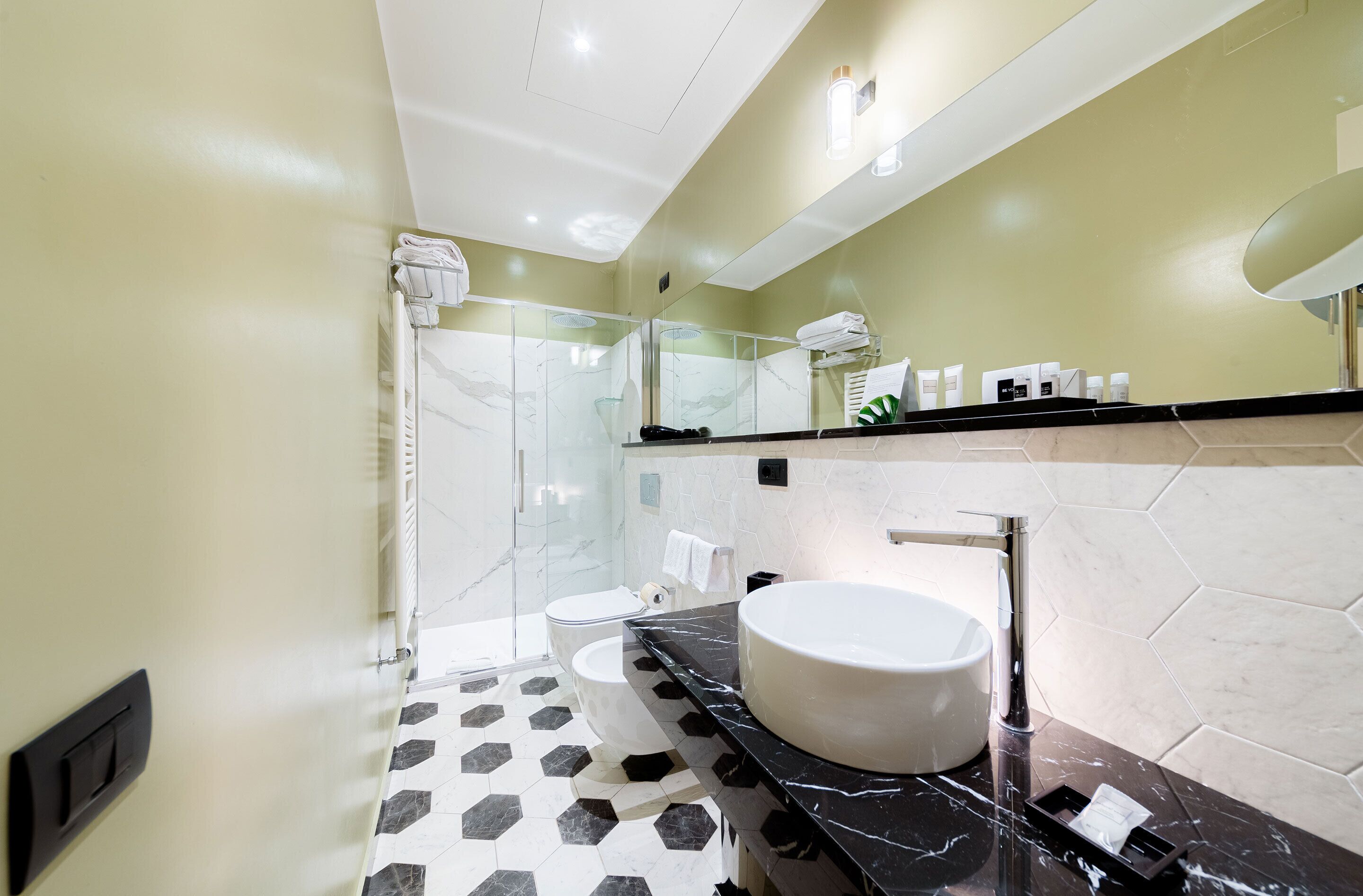 Un baño moderno con cabina de ducha de vidrio, lavamanos blanco y encimera de mármol negro.