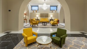 A lobby with a yellow sofa set, green armchairs, and a marble floor. - Hotel Astoria (Genoa)
