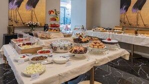 A buffet table with various food items and a vase of flowers. - Hotel Astoria (Genoa)