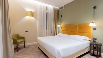 Quarto de hotel bem arrumado, com uma cama grande, uma cadeira pequena e duas luminárias fixadas na parede.