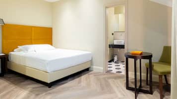 A hotel room with a bed, a small table, a chair, and a bathroom visible through an open door.