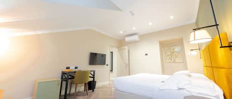 A hotel room with a bed, a desk, a chair, a small cabinet, a TV, and a wall-mounted lamp.