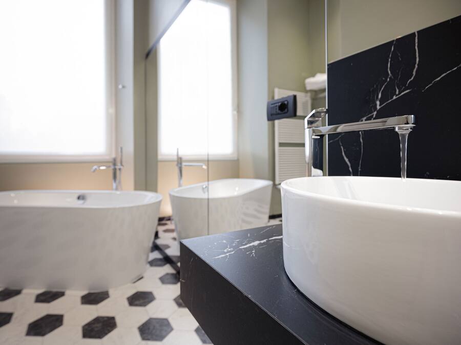 Un baño con dos tinas independientes, un tocador de mármol negro y un lavamanos blanco.