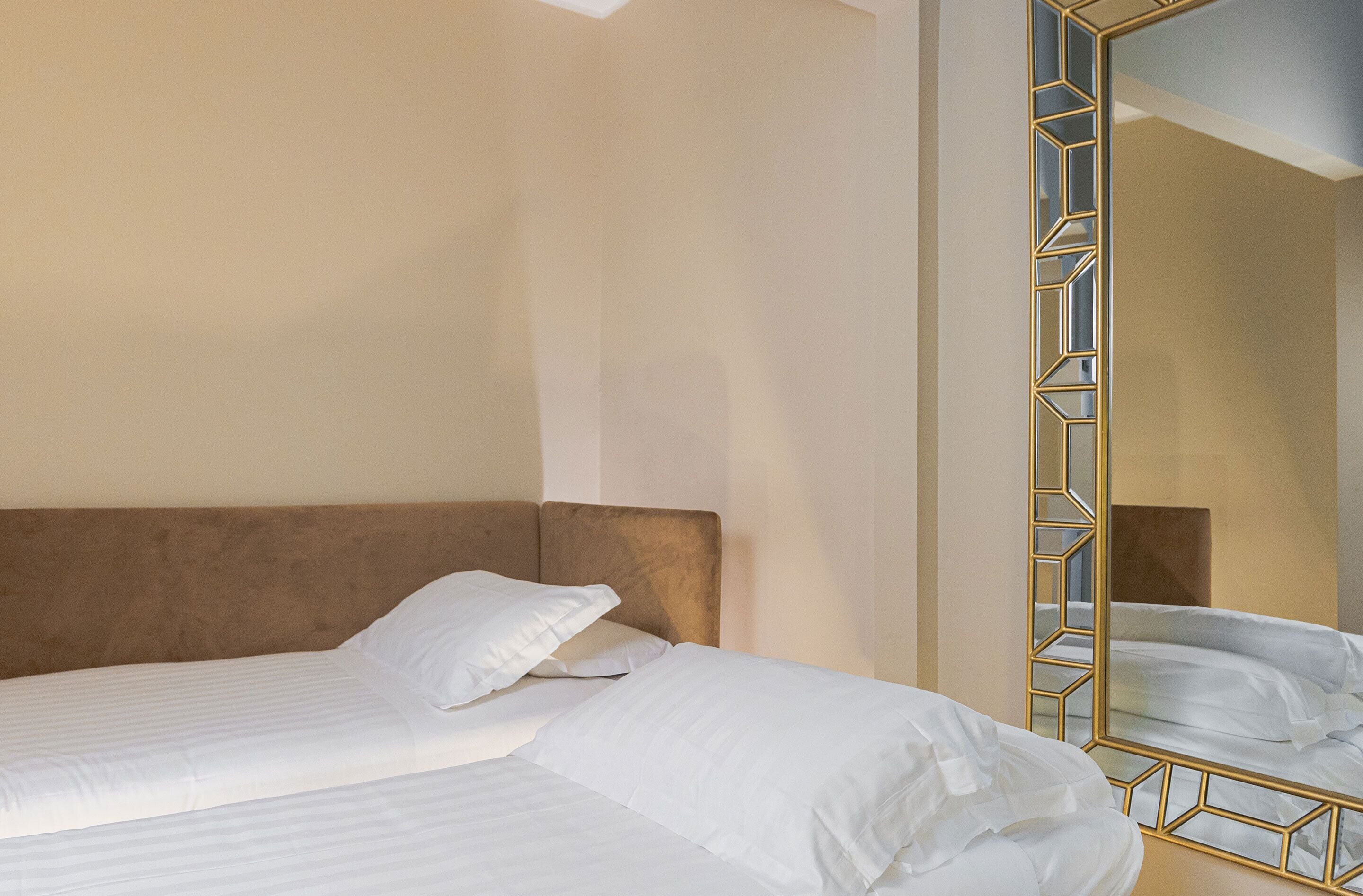 Une chambre d’hôtel avec un lit, une tête de lit et un miroir doté d’un cadre géométrique.