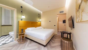 A hotel room with a bed, bedside table, lamp, TV, and a bathroom with a toilet and shower.
