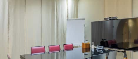 Un salón de conferencias con una mesa de vidrio, cuatro sillas rojas acolchadas, una pizarra y un televisor de pantalla plana grande.