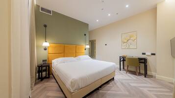 Une chambre d’hôtel comprenant un lit, une table de chevet, une lampe, un bureau, une chaise et une œuvre d’art accrochée au mur.