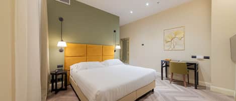 Habitación de hotel con cama, mesita de noche, lámpara, escritorio, silla y una obra de arte en la pared.