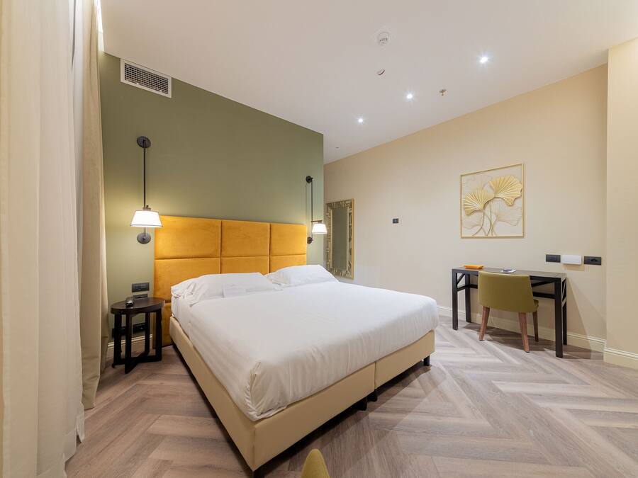Une chambre d’hôtel comprenant un lit, une table de chevet, une lampe, un bureau, une chaise et une œuvre d’art accrochée au mur.