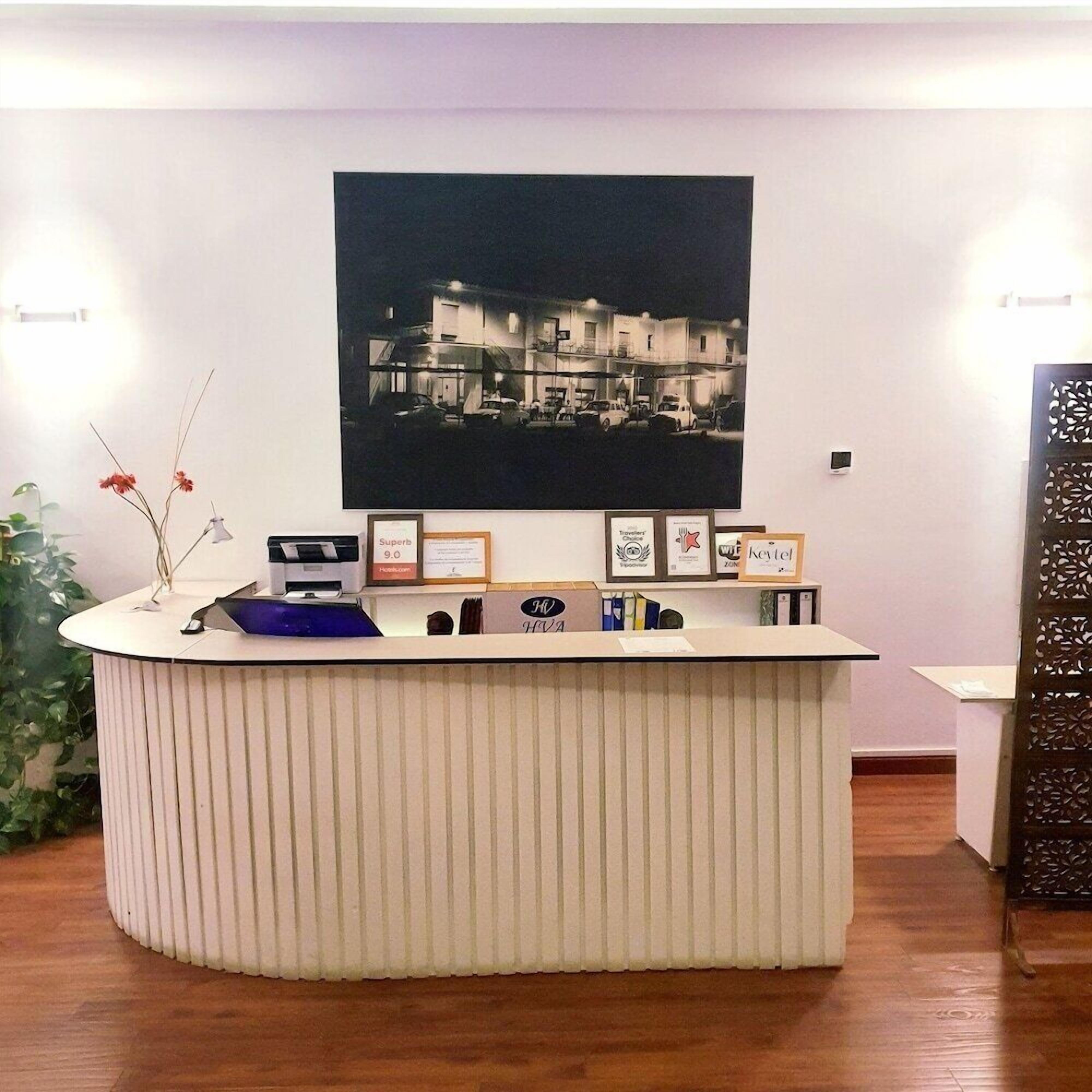 Un taulell de recepció amb una fotografia emmarcada a la part superior, una planta petita a l'esquerra i un panell decoratiu a la dreta.