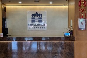 A reception desk with a sign for HOTEL ROYAL SINGAPORE, a digital display, and a framed certificate on the wall.