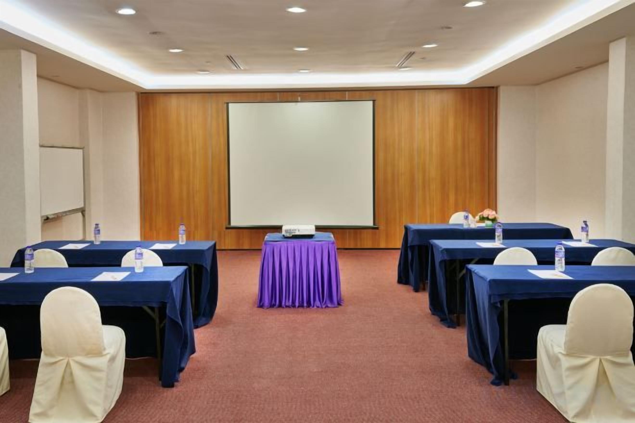 A conference room with tables, chairs, a projector screen, and a carpeted floor.