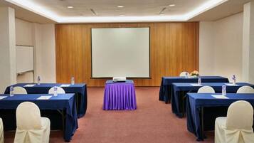 A conference room with tables, chairs, a projector screen, and a carpeted floor.
