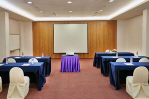 Un salón de conferencias con mesas, sillas, una pantalla de proyector y piso alfombrado.