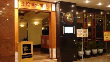A hotel entrance with a reception desk, a signboard, and potted plants.
