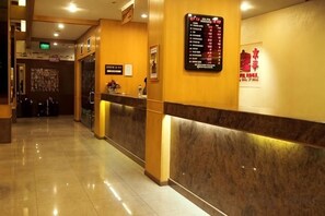 Zona de recepción de hotel con mostrador de mármol, un cartel con indicaciones y un panel de menú adherido a la pared.