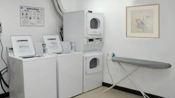 A laundry area with washing machines and an ironing board. Instructions are posted on the wall.