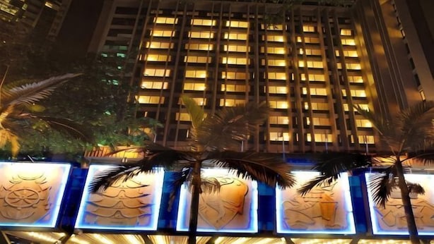 A high-rise building with illuminated windows at night, palm trees in front, and a series of illuminated panels with designs. - Hotel Royal Singapore (Singapore)