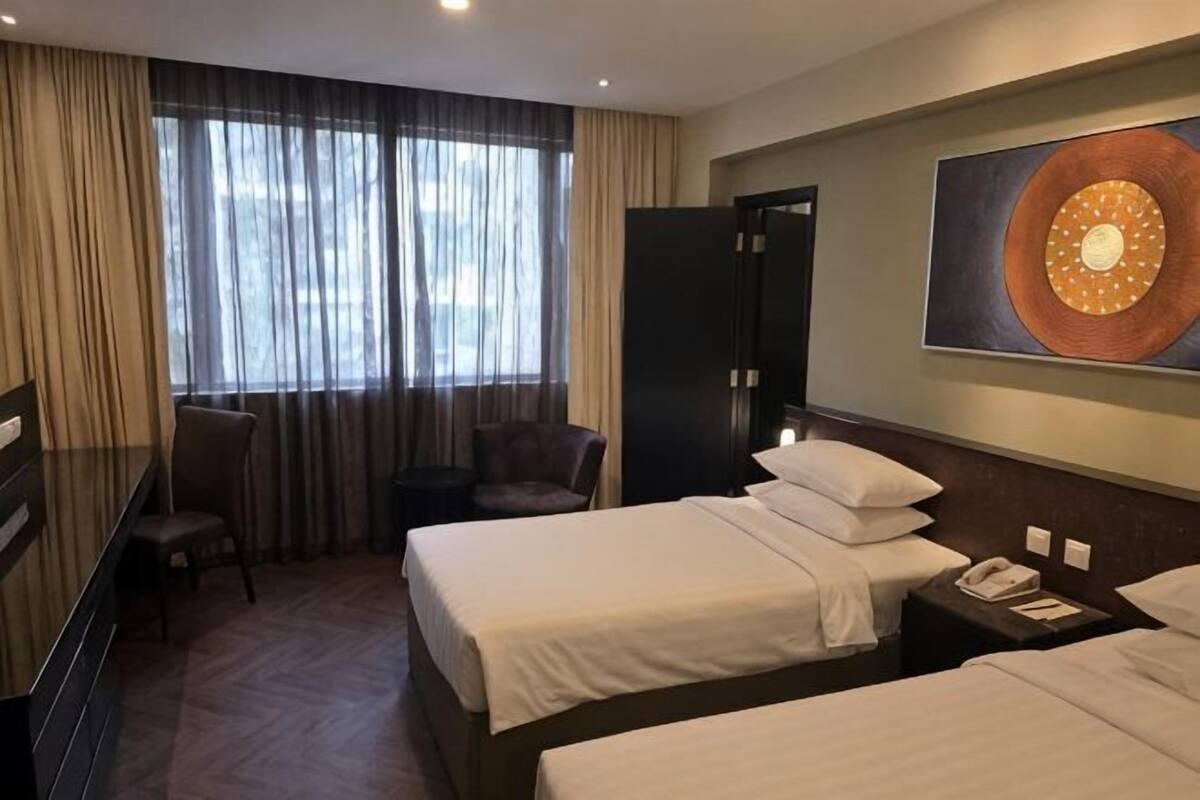 A hotel room with two beds, a desk, a chair, and a large window with curtains.