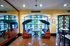 Un restaurante con una zona central de mesas y bancos acolchados, rodeado de amplias ventanas con vidrios de colores.