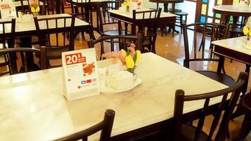 A restaurant interior with multiple tables and chairs, a menu stand, and a cake on one table.