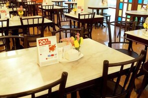 Un interior de restaurante con varias mesas y sillas, un expositor de menú y un pastel sobre una de las mesas.