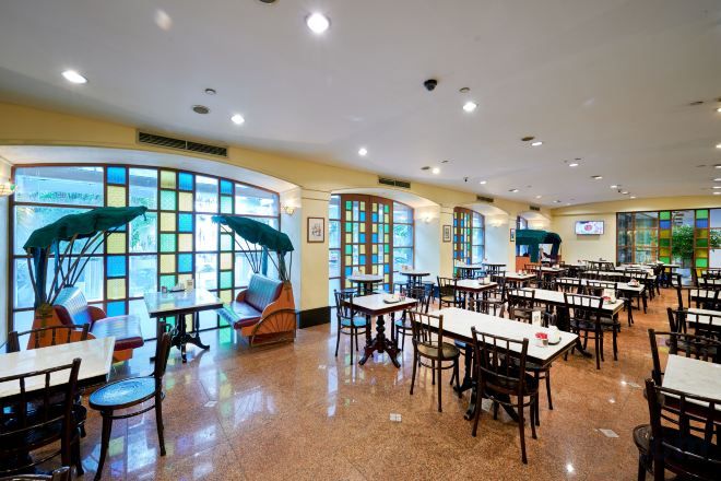 A spacious indoor dining area with multiple tables and chairs, large windows with view-enhancing curtains, and a ceiling with recessed lighting.
